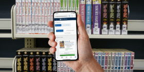 A hand holding a smartphone showing the CPL catalog in front of shelves of manga books